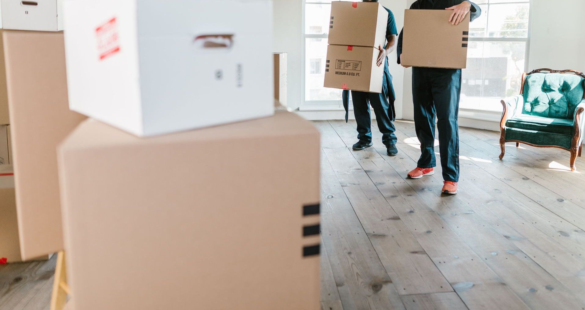Two movers in uniform carrying boxes in a bright, new home setting.
